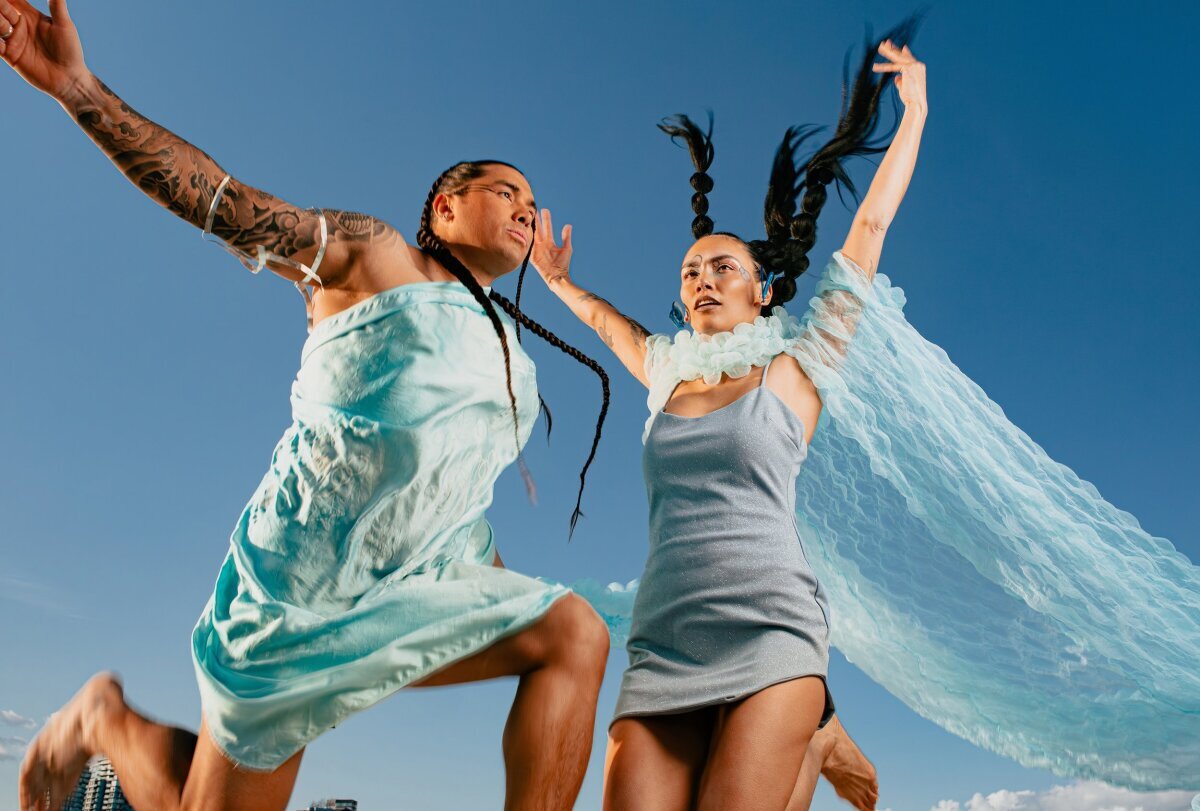 Image: Two models wearing blue clothing jumping with a blue sky background